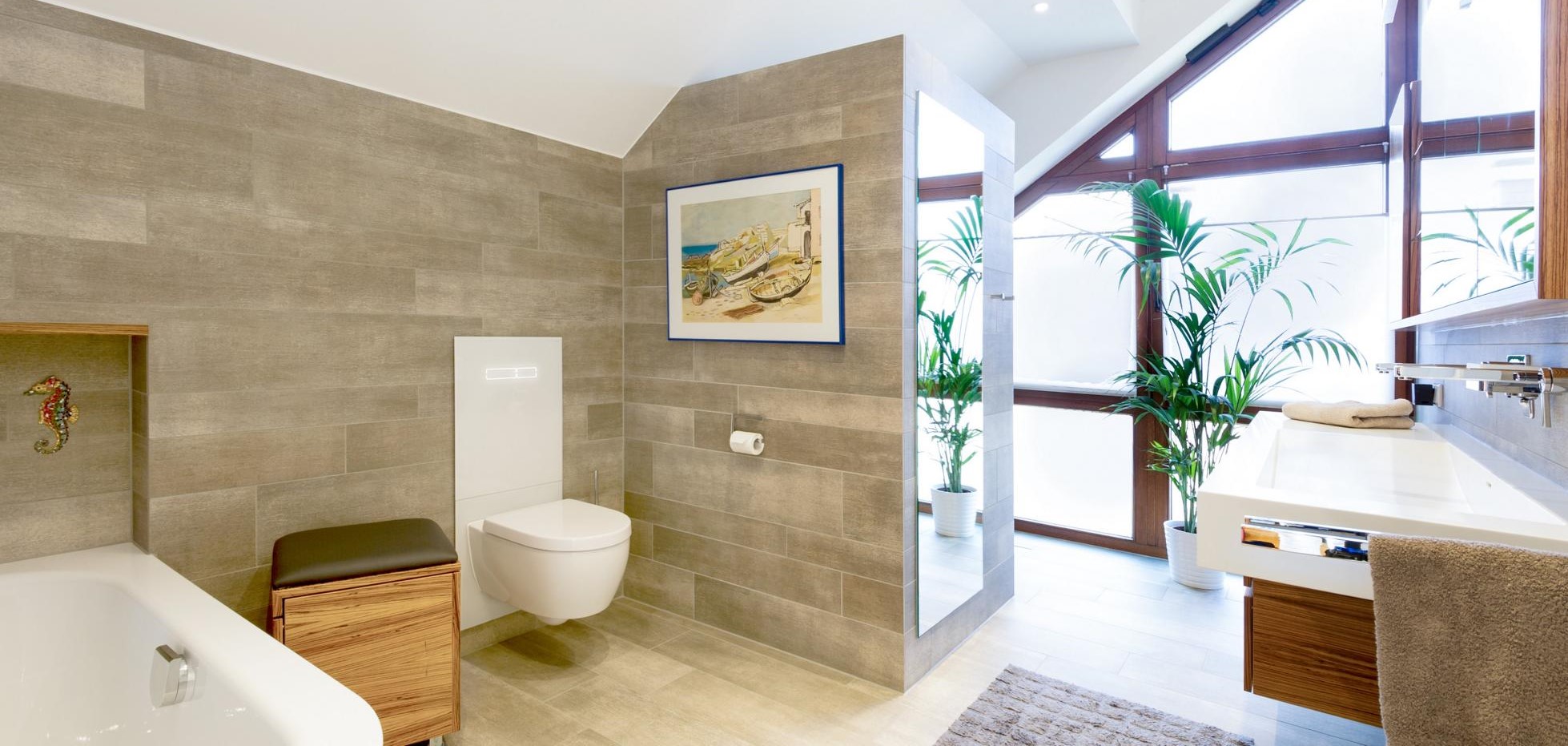 Badezimmer mit Natursteinfliesen, weißes WC, großes Fenster mit Palme davor.